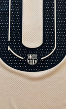 Load image into Gallery viewer, Close-up of a sports jersey with a logo on the chest against a dark blue and beige background. Yamal Kobe Barcelona
