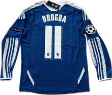 Load image into Gallery viewer, A long-sleeved royal blue soccer jersey with white stripes, featuring the name 'DROGBA' and the number '11' on the back. The jersey has Adidas branding and the Champions League patch.