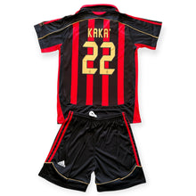 Load image into Gallery viewer, A black and red striped soccer jersey and matching shorts set. The back of the jersey features red and black vertical stripes, gold lettering reading 'KAKA' and the number '22', and gold piping details.