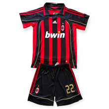 Load image into Gallery viewer, A children's AC Milan soccer kit consisting of a short-sleeve jersey and matching shorts. The jersey features red and black vertical stripes with thin gold stripes, a white Adidas logo on the right chest, a white 'bwin' sponsor logo across the center, and the AC Milan club crest on the left chest.