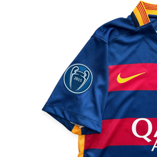 Load image into Gallery viewer, Close-up of a blue FC Barcelona soccer jersey with red and yellow horizontal stripes, featuring the 2015 Champions League patch on the sleeve and a yellow Nike swoosh on the chest.