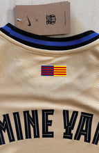Load image into Gallery viewer, Beige sports jersey with black and blue stripes and a flag patch, on a beige background. Kobe Yamal Barcelona Neck view

