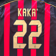 Load image into Gallery viewer, Close-up of the back of an AC Milan jersey with red and black vertical stripes, gold lettering reading 'KAKA', and the number 22 outlined in black.

