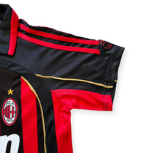 Load image into Gallery viewer, Close-up of a black and red striped soccer jersey with gold trim, featuring the AC Milan crest on the chest.
