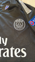 Load image into Gallery viewer, Black sports jersey with Paris Saint-Germain logo and visible branding on a beige background
